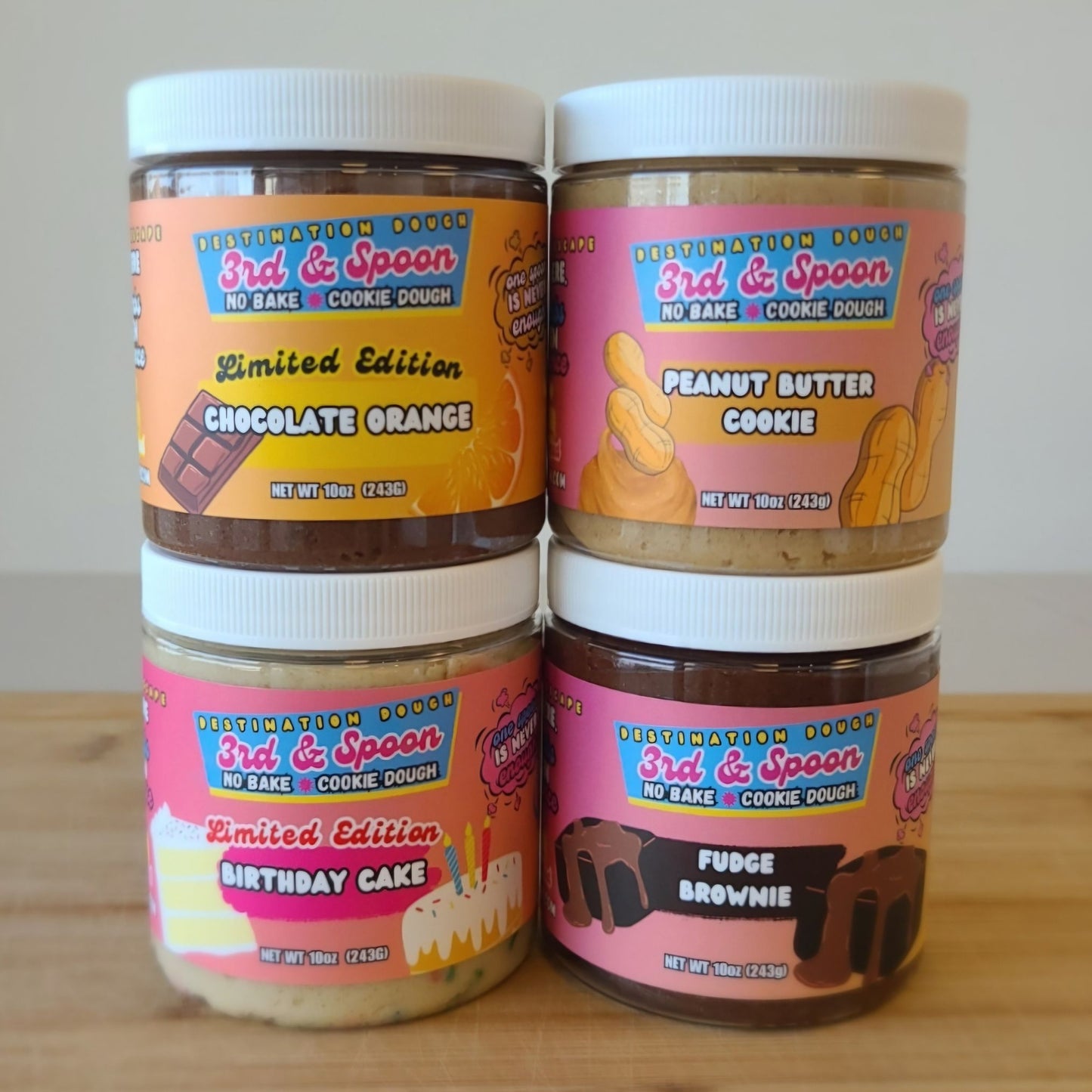 Four 10oz jars of 3rd & Spoon no bake cookie dough with colorful labels on a wooden surface.