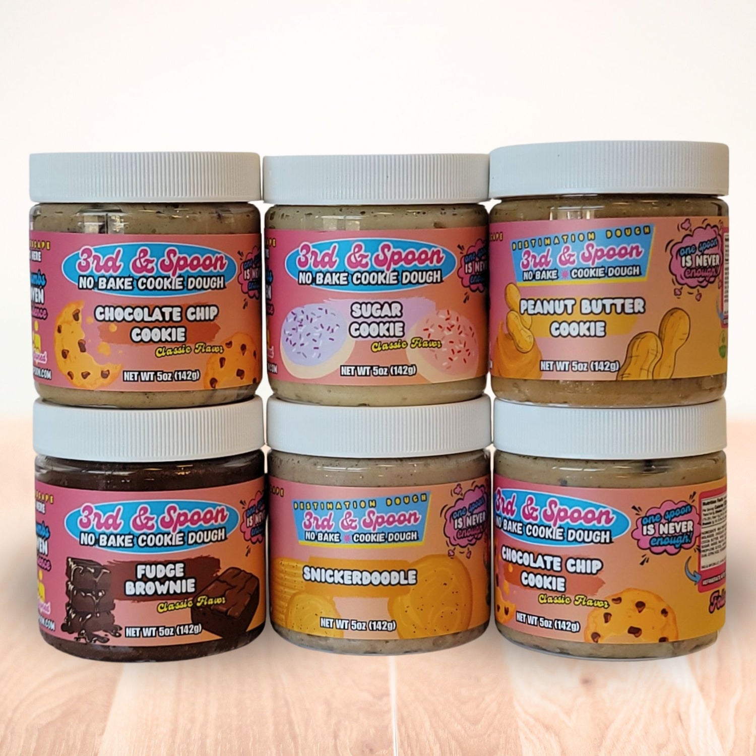 Six small jars of 3rd & Spoon edible cookie dough with various flavors on a light background.